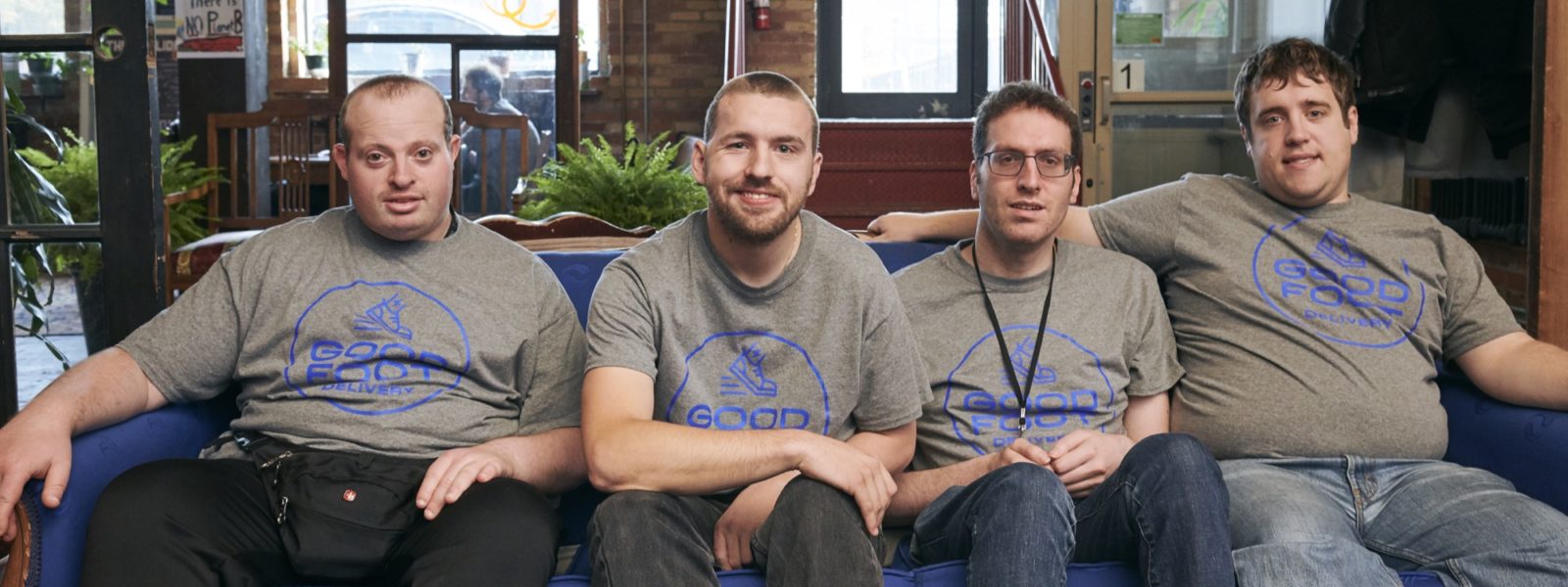 Four smiling Good Foot Delivery couriers seated on a couch